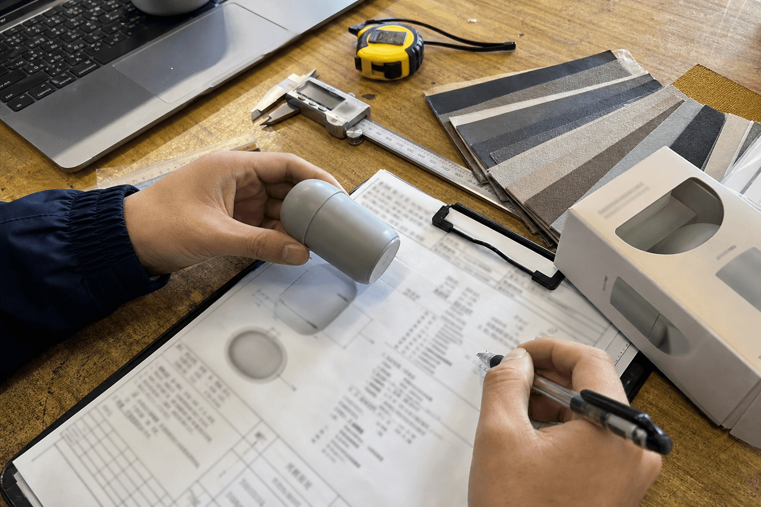 Hands measuring an unbranded sample beside blurred product specification notes and material swatches
