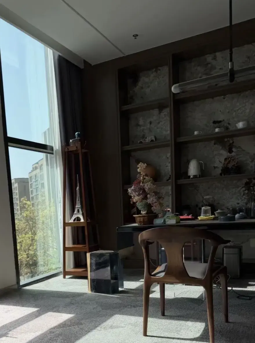 Office with a floor-to-ceiling window, bookshelves, a desk and a wooden chair.