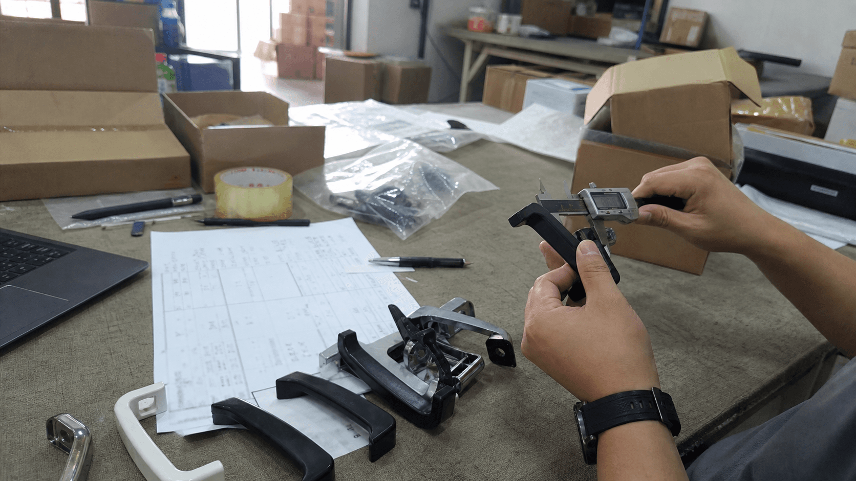 Hands measuring product samples with calipers on a cluttered China sourcing review desk